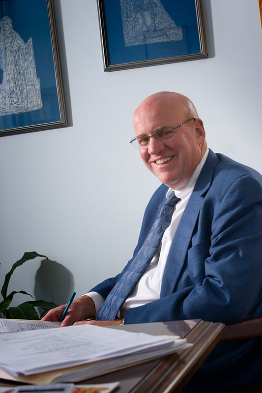 Image of David Hillier at his desk reviewing documents smiling at the camera.