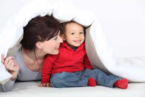 Image of a woman playing with a baby under a white coverlet depicting the idea of adoption.