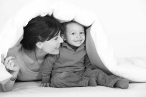 Image of a woman playing with a baby under a white coverlet depicting the idea of adoption.