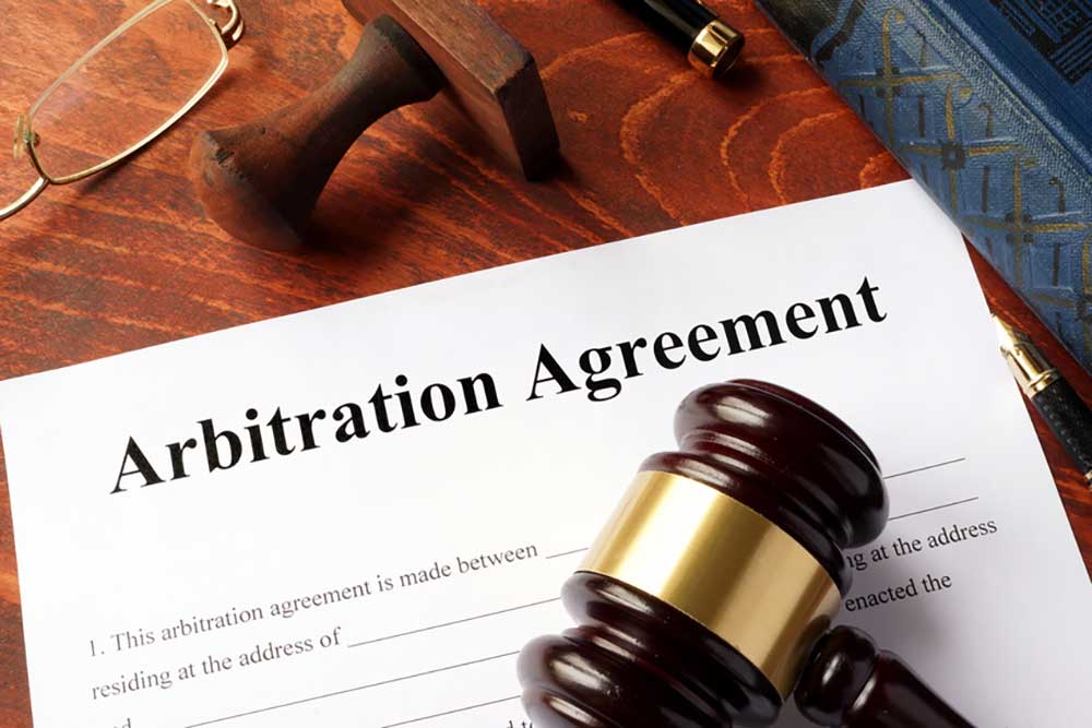 Image of an incomplete arbitration agreement on a wooden desk with lawyerly things, a pen, a stamp, reading glasses, a law book and a gavel.