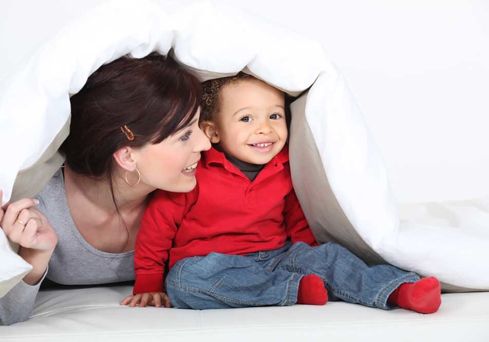 Adoption Image of a woman playing with a baby under a white coverlet depicting the idea of adoption.