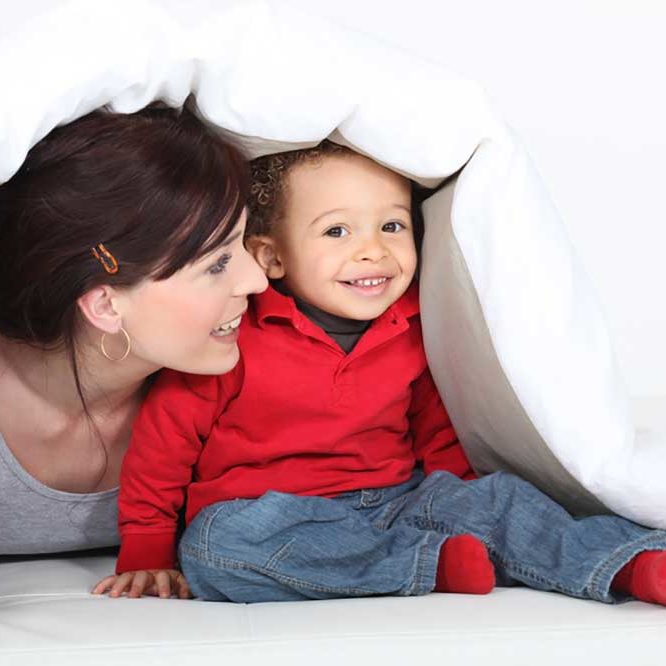 Image of a woman playing with a baby under a white coverlet depicting the idea of adoption.