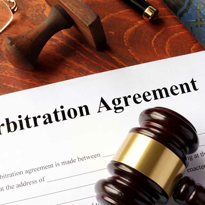 Image of an incomplete arbitration agreement on a wooden desk with lawyerly things, a pen, a stamp, reading glasses, a law book and a gavel.