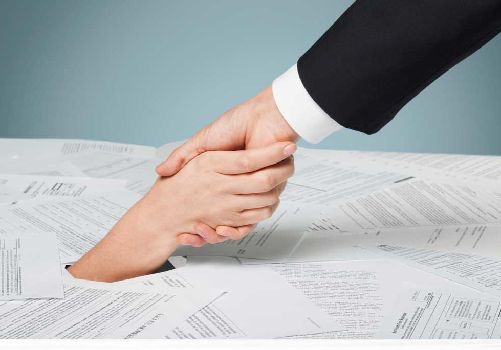 Bankruptcy Paperwork Image depicting drowning in paperwork, scattered forms with one person pulling another out from under it