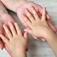 Image of small child with hands, palms face down, in the hands of an adult, depicting child support
