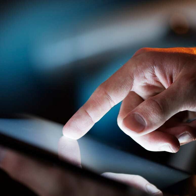 Man's hands holding and using a backlit digital tablet in low light ambience room