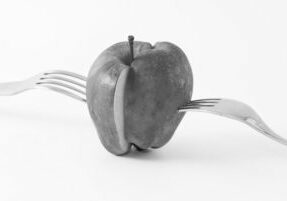 Black and white image of an apple sliced in half with forks protruding from each of the halves denoting equal distribution and splitting of marital property