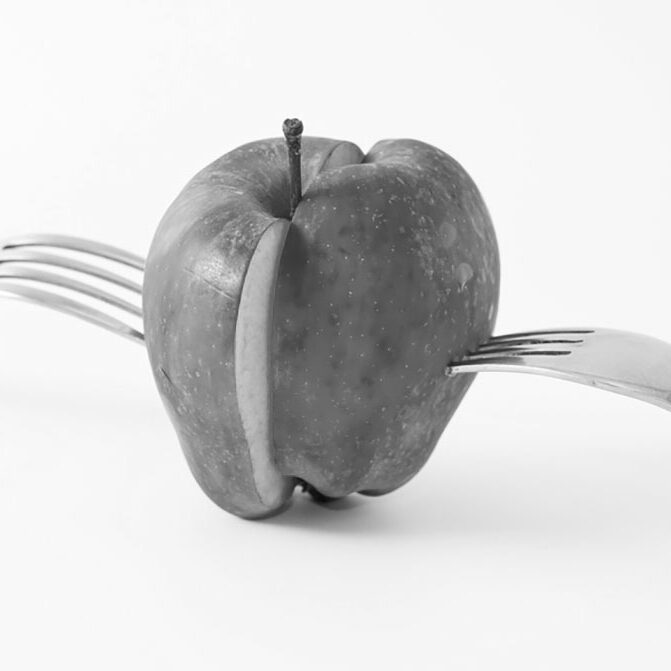 Black and white image of an apple sliced in half with forks protruding from each of the halves denoting equal distribution and splitting of marital property