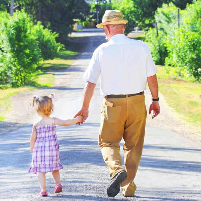Photograph of a grandfather and preschool granddaughter walking away on a wide path through a path