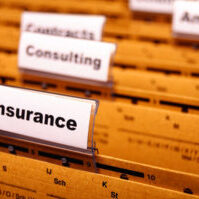 Image taken from across the top of a filing cabinet drawer with hanging file folders with plastic tab separators. The foremost forward tab is labeled "Insurance" while remaining tabs are slightly out of focus.