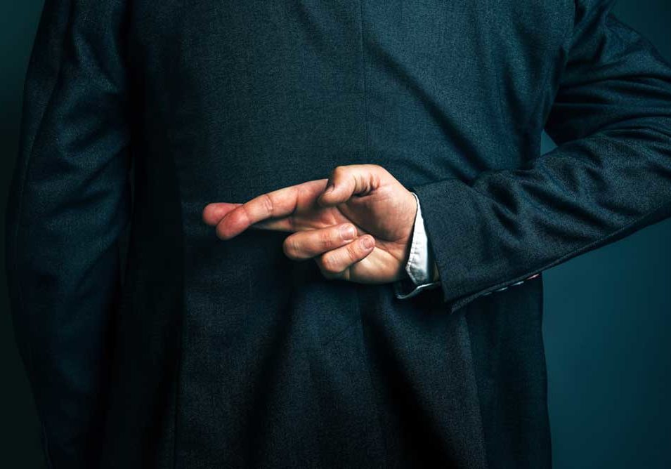 Liar Image of the back of a man in a suit with his right arm bent behind his back and his fingers crossed, depicting the act of a lie.