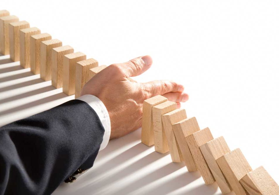 Mediation Image of dominos in a single row, split by a man's hand. The left side of the row is protected from the right, which is teetering over, representing how mediation can help protect what remains from being lost.