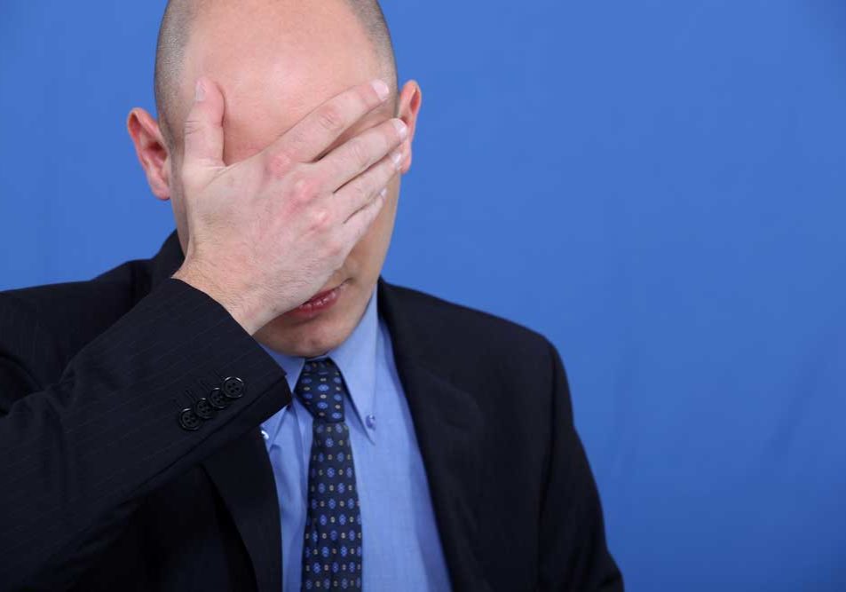 I made a mistake Image of man standing on a blue background with his hand over his forehead as if ashamed of the mistake he has made.