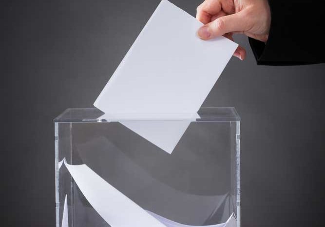 Suggestions Image of a person dropping a card into a clear glass container, like a suggestion box or ballot bowl.