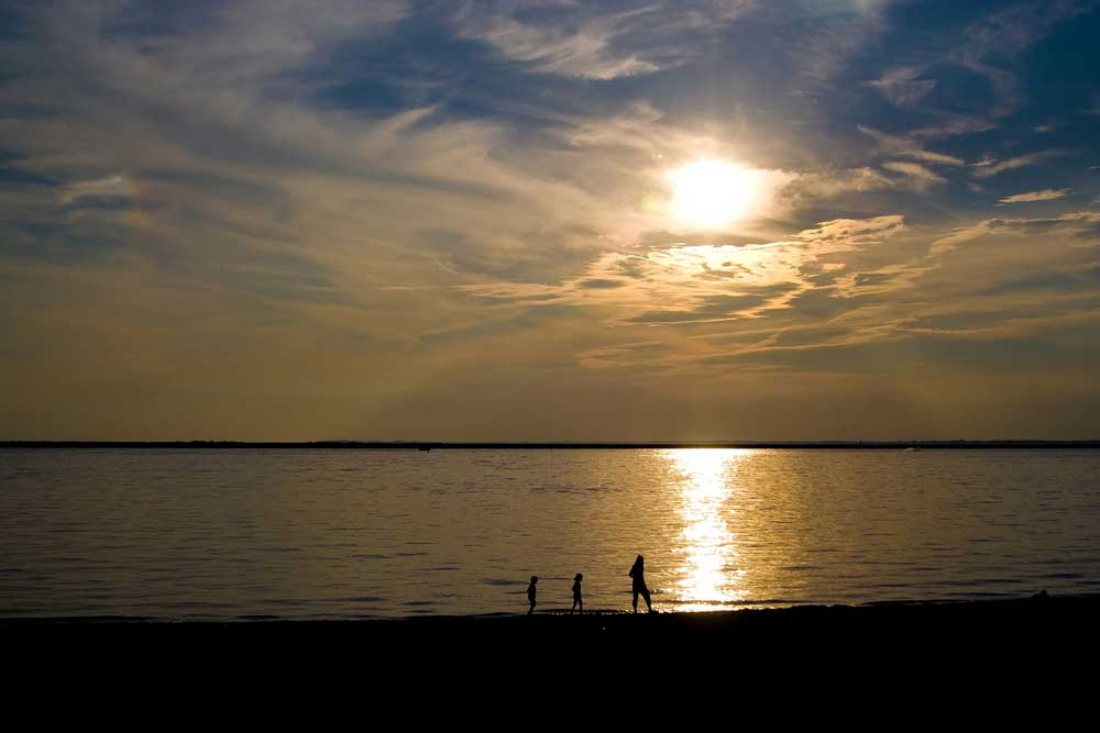 Single parent and two small children walking on the distant beach at dusk in silhouette.