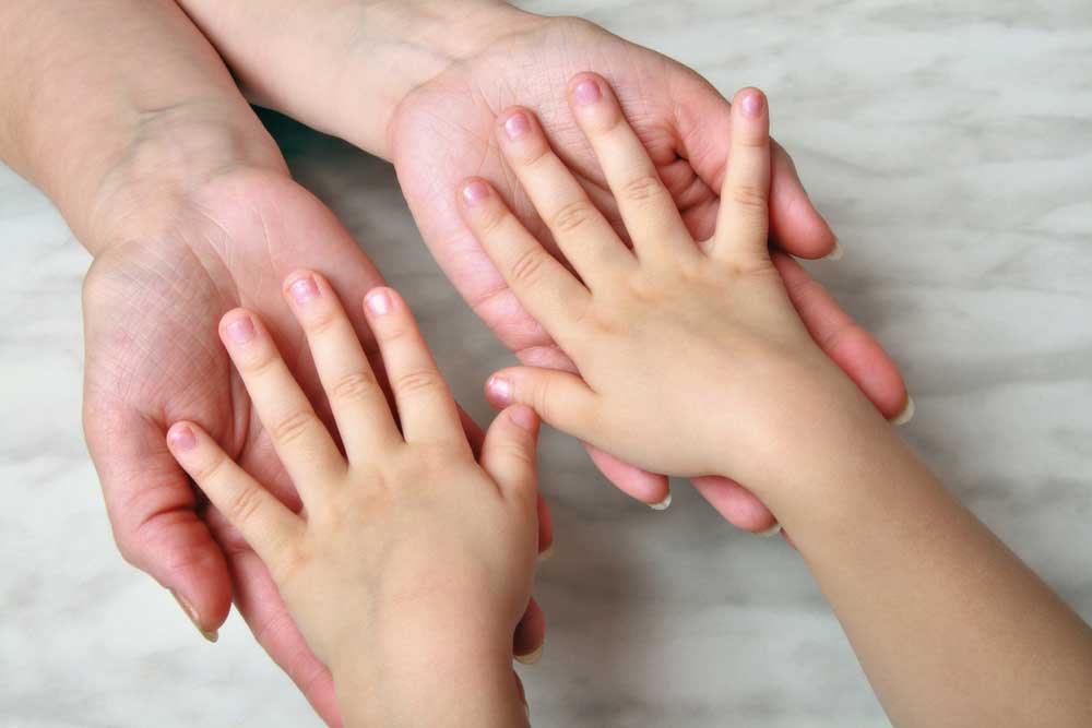 Image of small child with hands, palms face down, in the hands of an adult, depicting child support