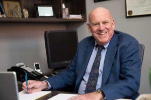 Image of David R. Hillier smiling at the camera from behind his desk.