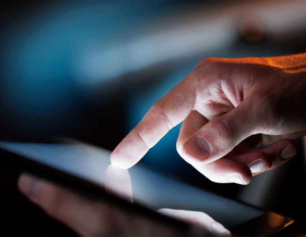 Man's hands holding and using a backlit digital tablet in low light ambience room