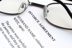 Image of a typewritten agreement for divorce on white paper with a pair of eyeglasses folded on top of it.