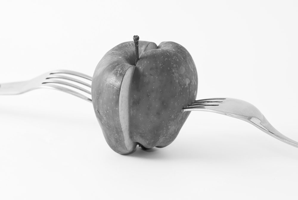 Black and white image of an apple sliced in half with forks protruding from each of the halves denoting equal distribution and splitting of marital property