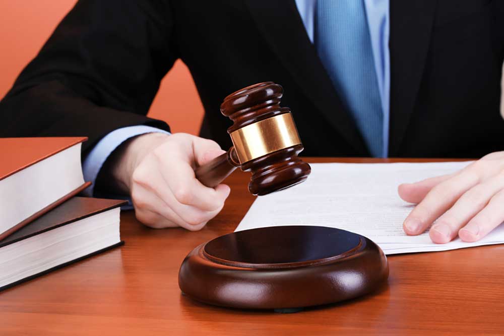 Image of a man in a black suit and blue tie, cropped without a face, pounding a gavel.