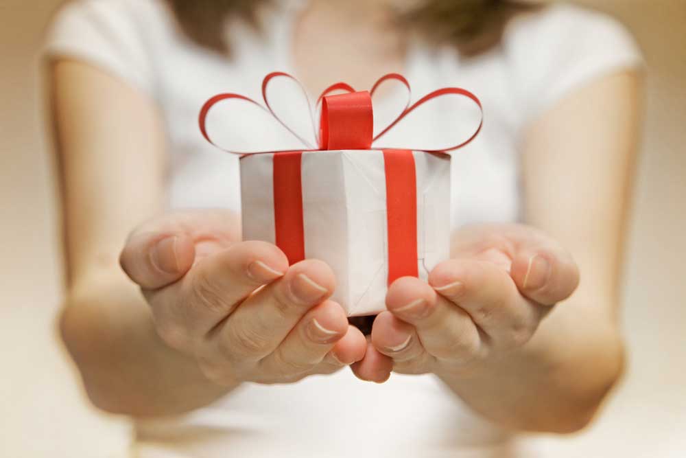 Image of a woman with her hands held together in front of her holding a small white package with a red bow.