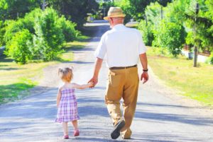 Photograph of a grandfather and preschool granddaughter walking away on a wide path through a path