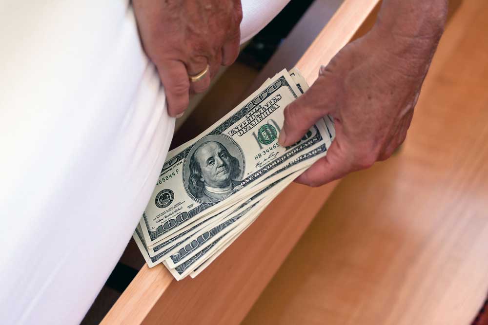 Picture of a man's hands wearing a wedding ring hiding money under the mattress.