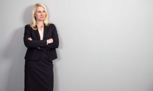 This image is Janet Amburgey's website biography image. It depicts Janet standing against a gray wall in their newly designed and renovated offices in historic downtown Asheville.
