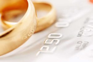 Closeup image of a credit card with wedding rings on the top of it depicting marital debt.