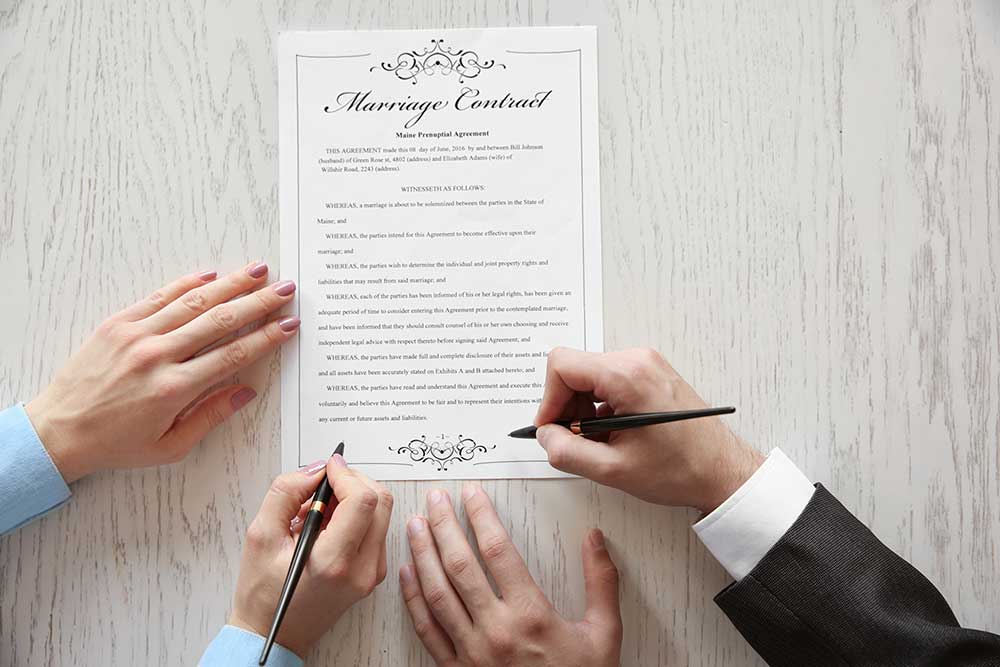 Stock photography image of a Marriage Contract on a table with the hands of a man and a woman signing it.