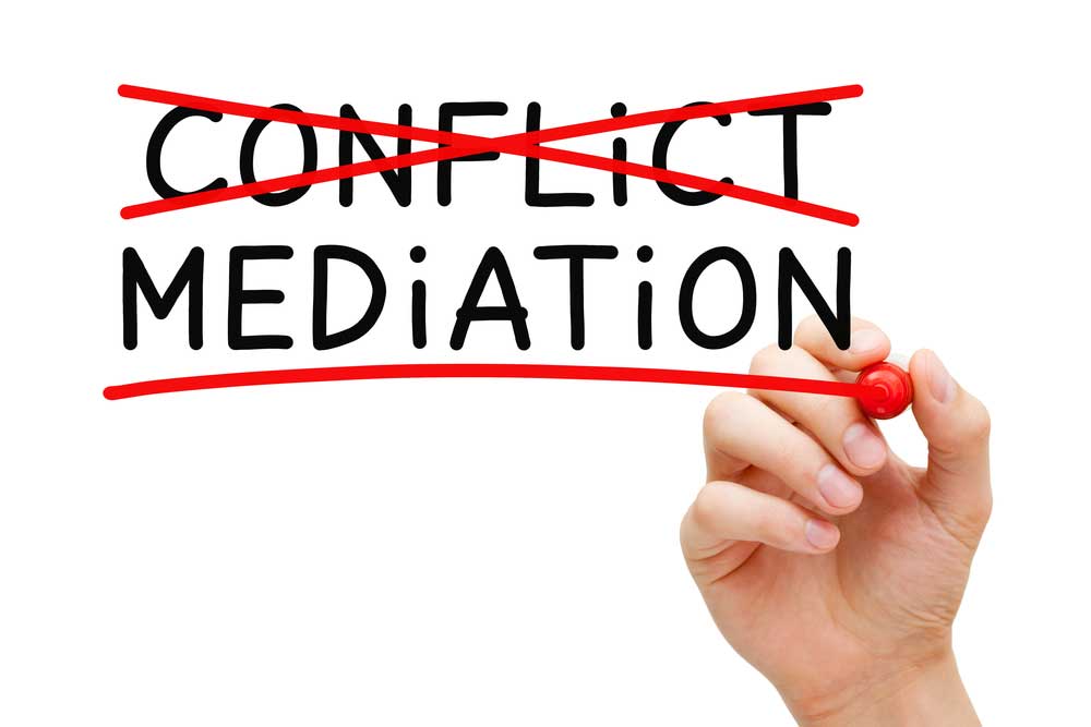 Conflict Resolution image depicting the words "conflict" and "mediation" on a glass board. Person with red marker has crossed out "conflict" and is underling mediation.