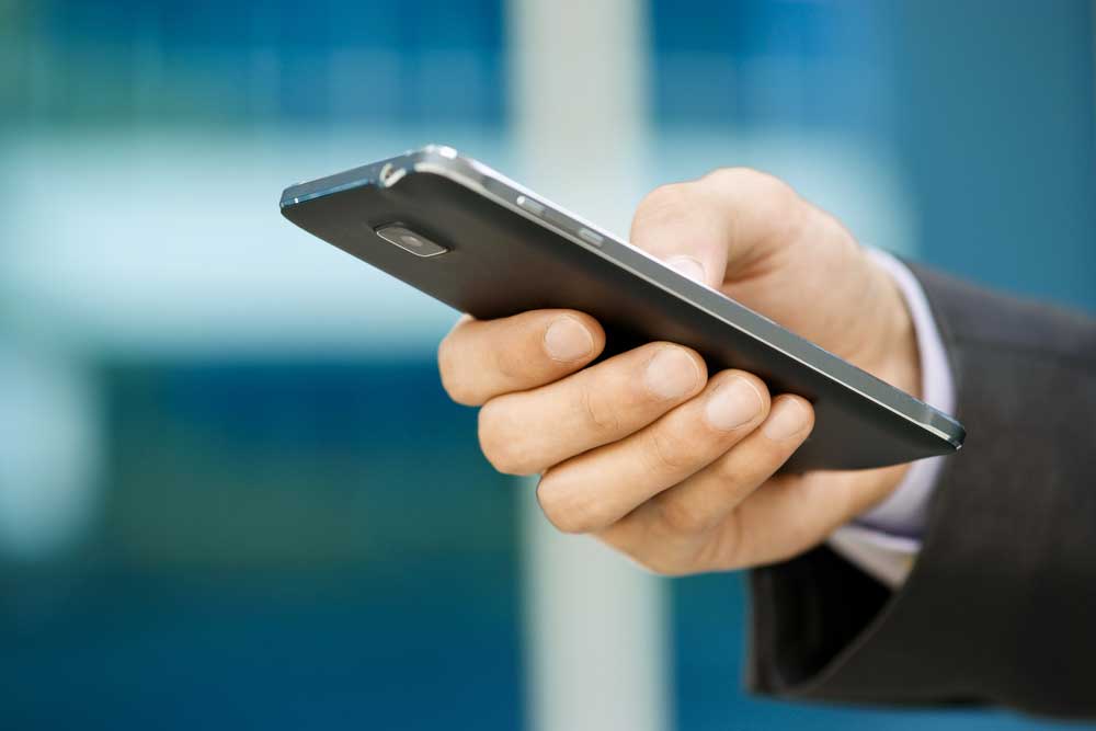 Image of a man's hand using a mobile phone in a corporate atmosphere.