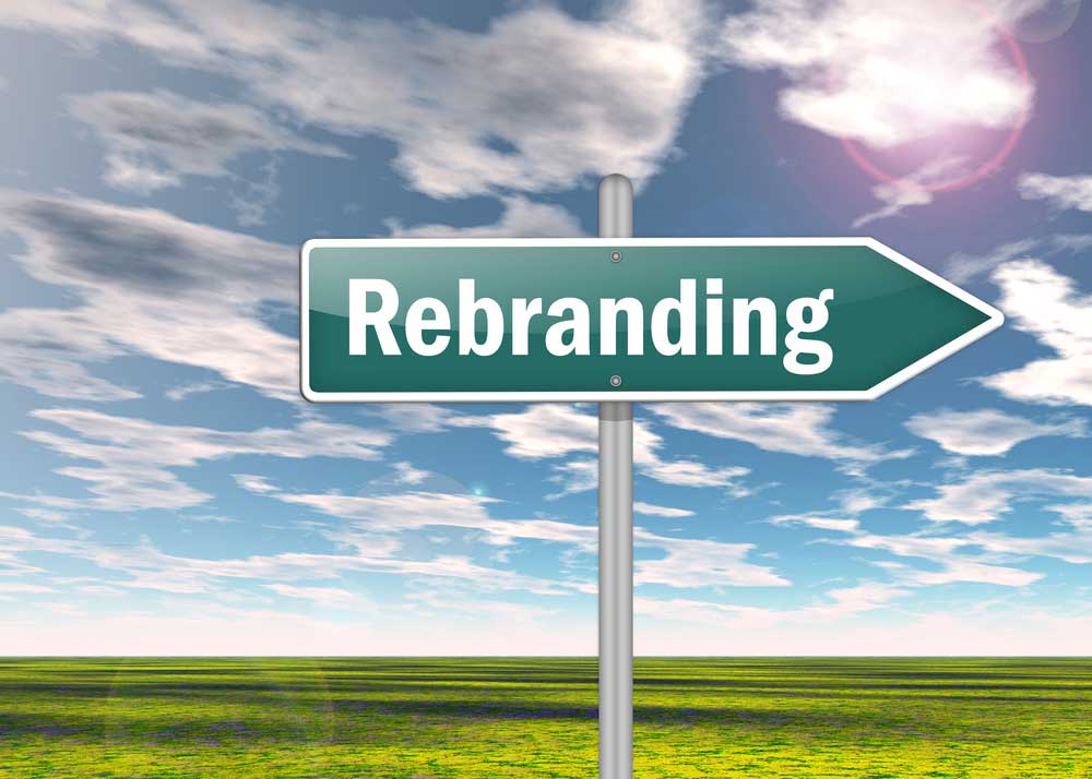 Street sign against a cloud dappled sky above a grassy field that says "Rebranding" depicting changing a name and identity