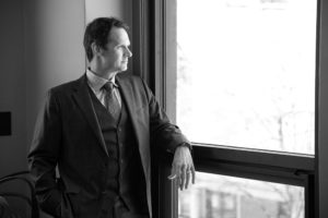 Black and white image of Patrick McCroskey looking out the window in his top-floor office at the newly renovated historic 47 North Market Street building owned by the firm for decades.