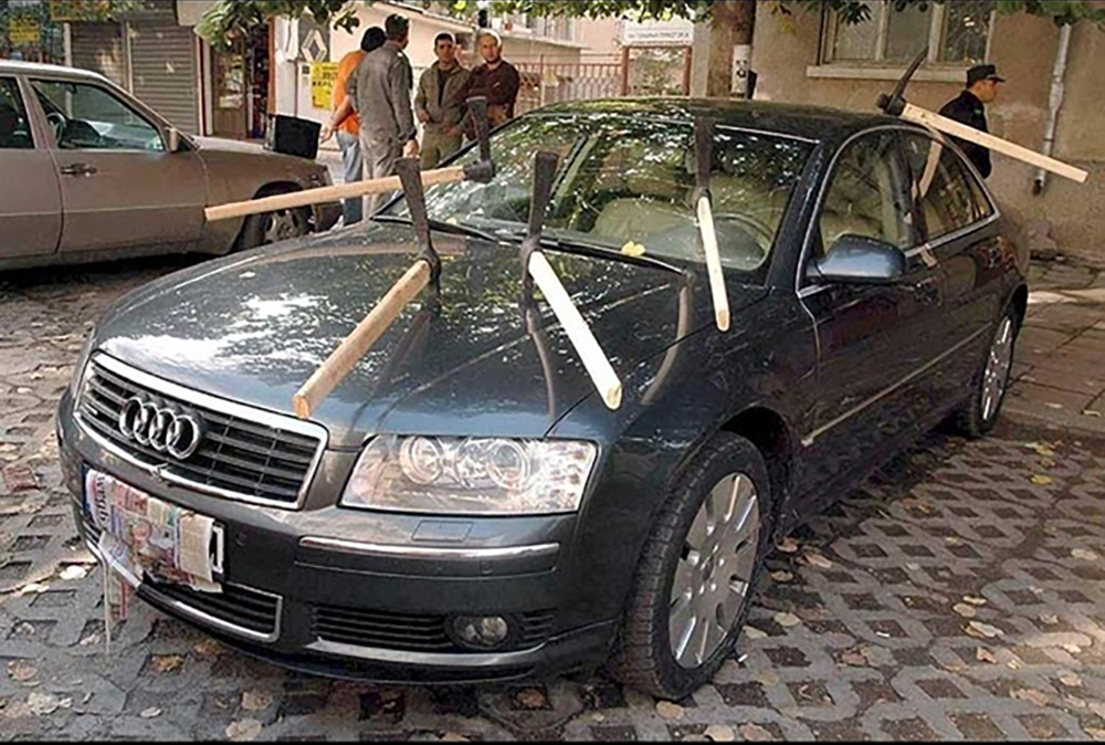 Image of an Audi sedan with six pick axes stuck into it depicting revenge in divorce. Ouch.