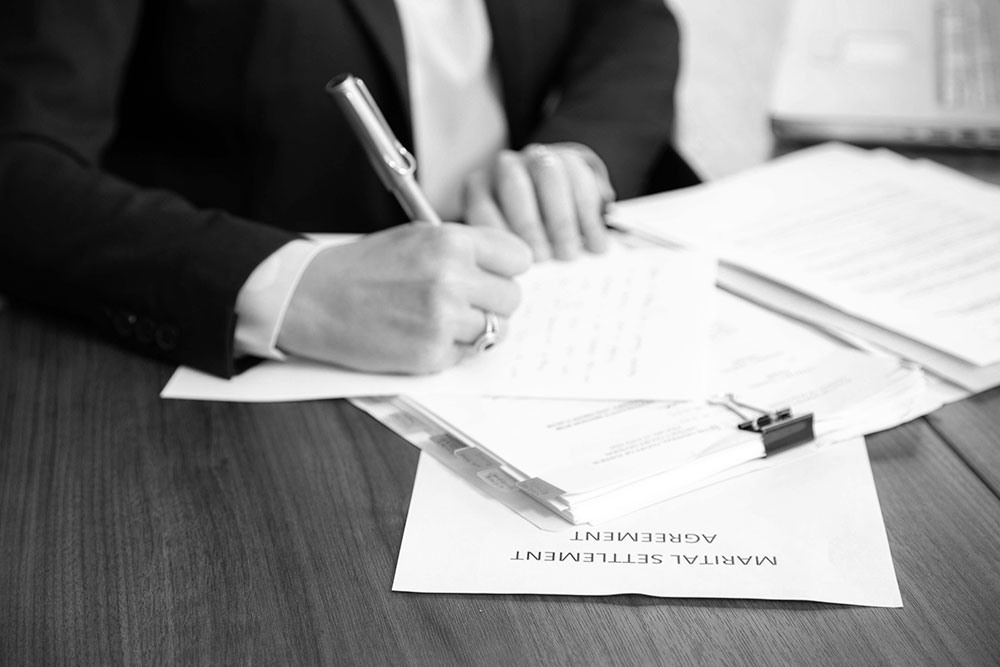 Black and white custom stock photography image of Janet Amburgey working at her desk making notes on a marital settlement agreement file.